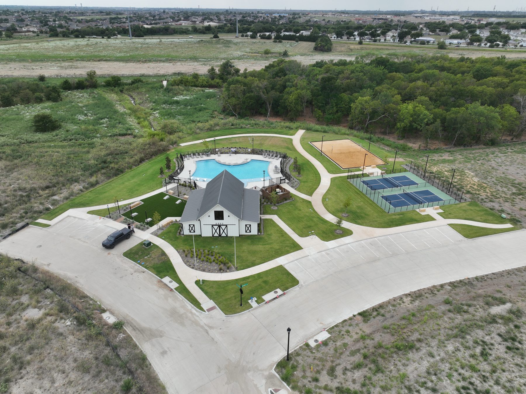 Aerial view of the amenity building, pool, pickleball courts, and sand volleyball court at Liberty Crossing in Royse City, Texas