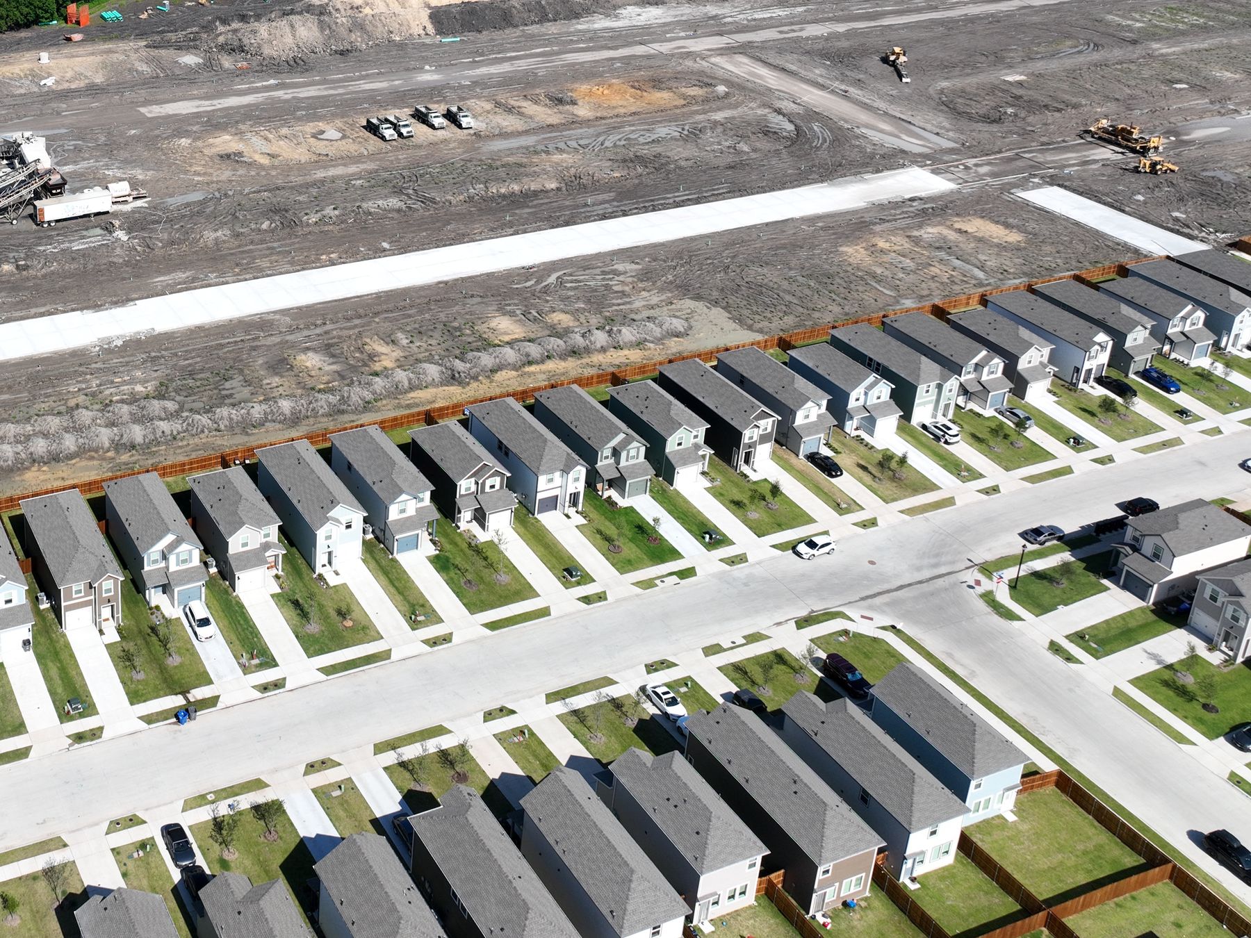 Aerial view of a street of finished two-storey homes at Arbor Trails Phase 1 in Princeton, Texas, beside the next phase being paved
