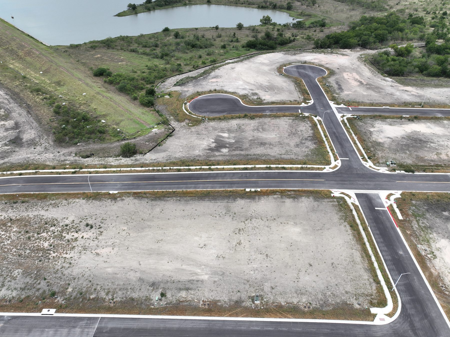 Aerial view of finished streets and homesites beside a pond at Prairie Lakes Section 3 in Kyle, Texas