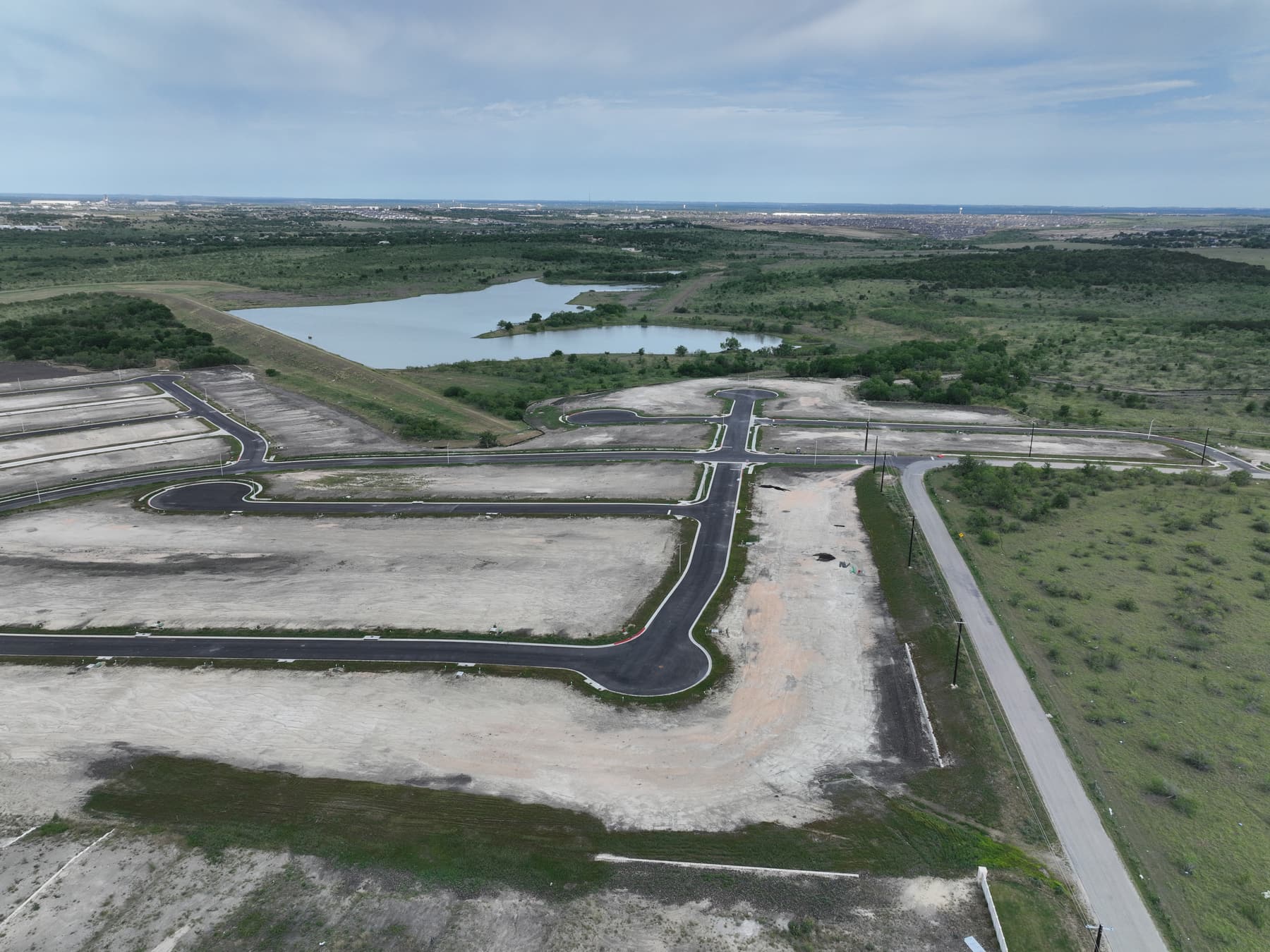 Aerial view of finished streets and homesites at Prairie Lakes in Kyle, Texas, beside a pond