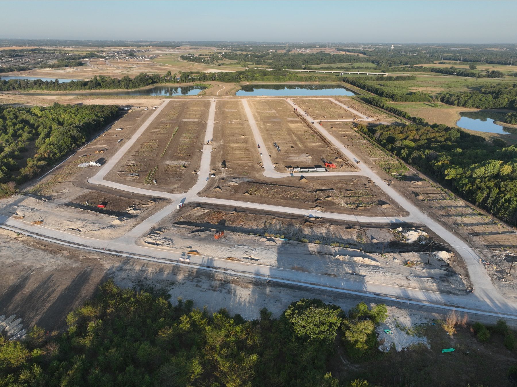 Aerial view of newly paved streets and graded homesites at Riverstone Estates in Melissa, Texas, with ponds and woodland beyond