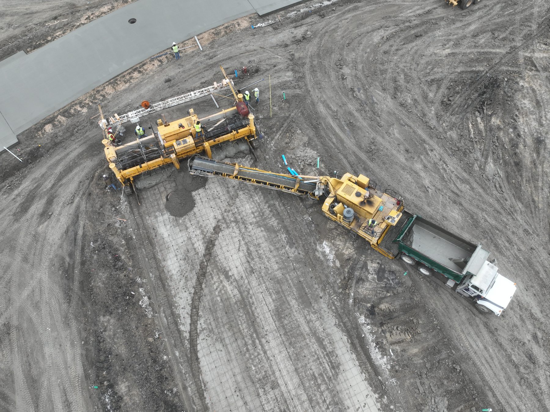 Aerial view of a slipform paver being charged by a concrete truck on a new street at Arbor South in Princeton, Texas
