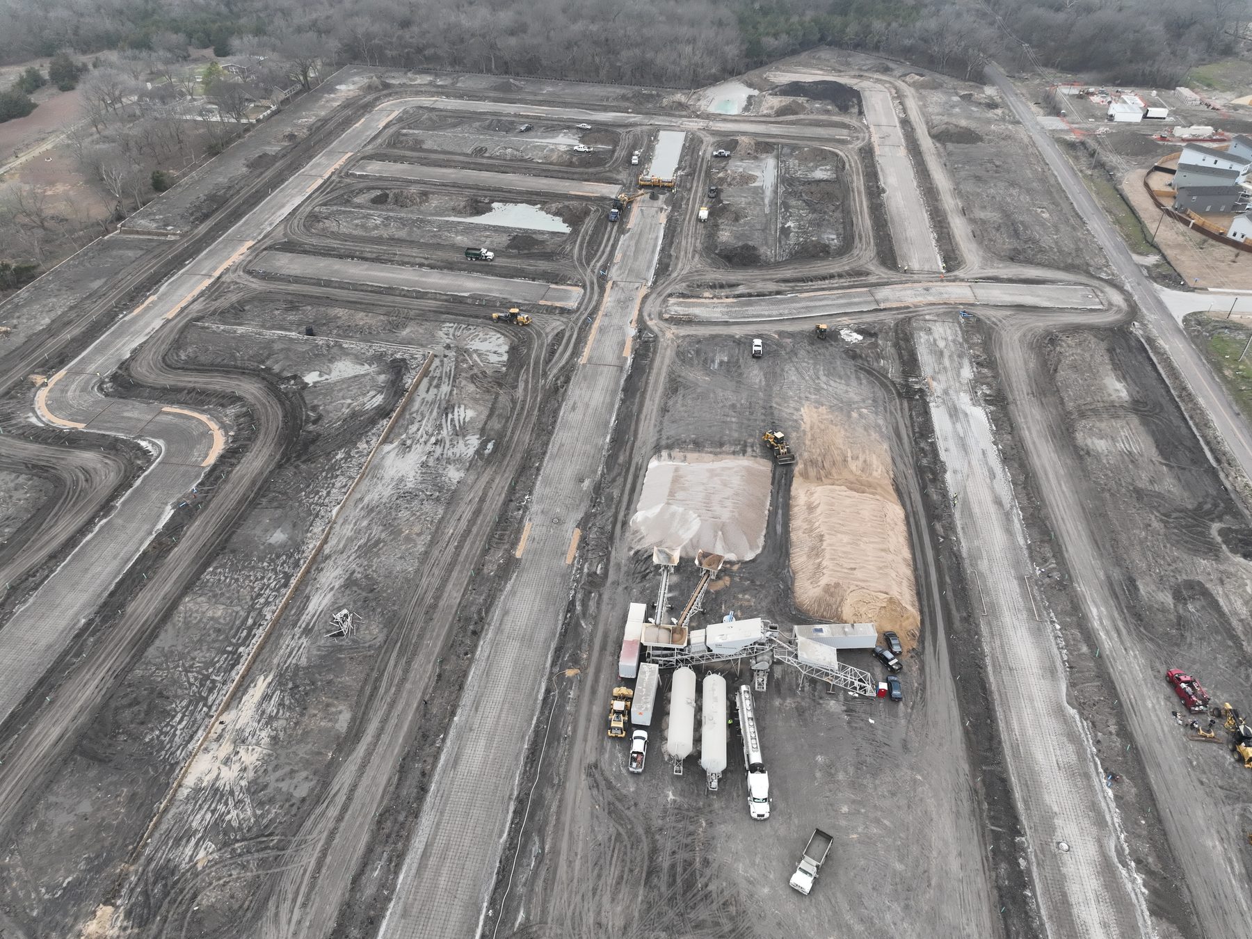 Aerial view of cement tanker trailers and material stockpiles staged on site ahead of paving at Arbor South in Princeton, Texas